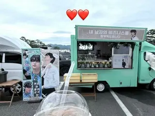 นักแสดงบยอนวูซอกทำรูปหัวใจคู่หนึ่งขณะถือเครื่องดื่มเป็นของขวัญจากรถคาเฟ่